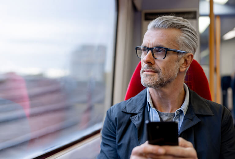 Man holding smart phone looks out of train window